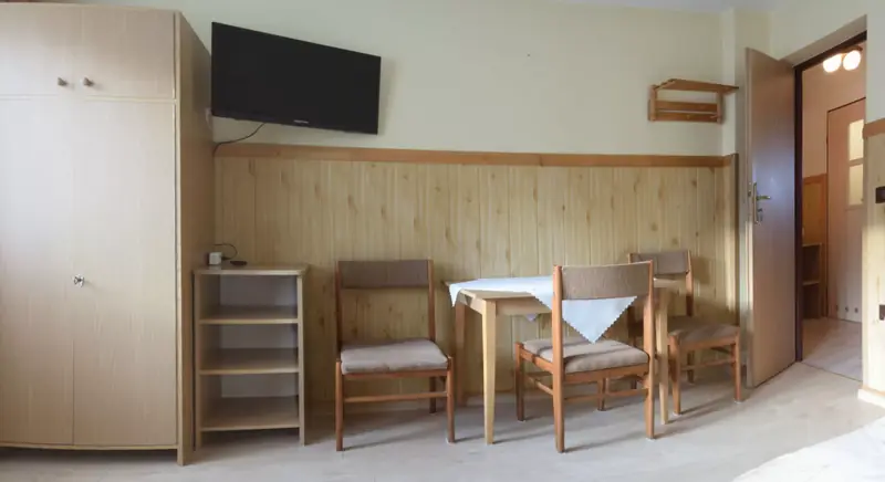 Szafa, telewizor, stół i krzesła w pokoju trzyosobowym
